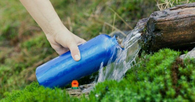 What to Look for in a Water Bottle — Woman Filling Water Bottle from Stream on Hiking Trip.